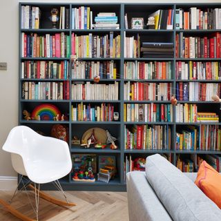 A living room with a white rocking chair and a blue shelving unit housing books and kids' toys