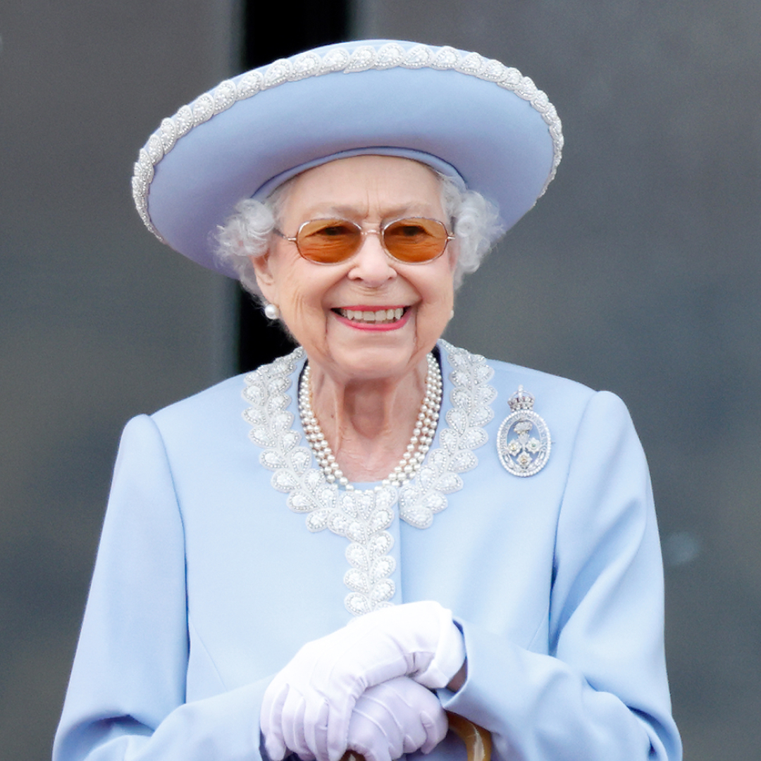 Queen Elizabeth smiling in a blue coat and wide brimmed hat