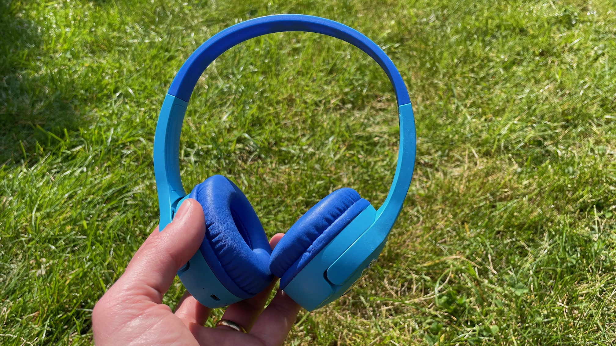 A blue pair of Belkin SoundForm Mini kids' headphones held in front of some lawn.