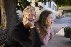 Grandfather and granddaughter leaning on garden table.