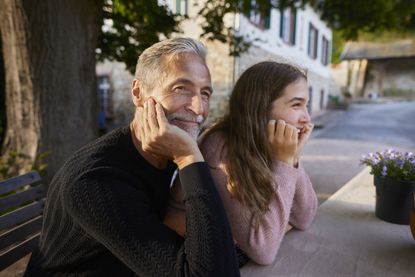 Grandfather and granddaughter leaning on garden table.