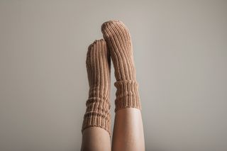 A pair of legs in the air with cosy, brown, knitted socks on.