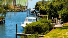 A canal view of Sarasota, Florida with lush green lawns, hedges, trees and white boats on the blue water.