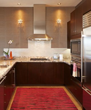 A red and brown kitchen with white countertops and wall sconces