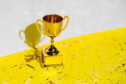 Golden champions cup standing on yellow background with glitter and confetti. 
