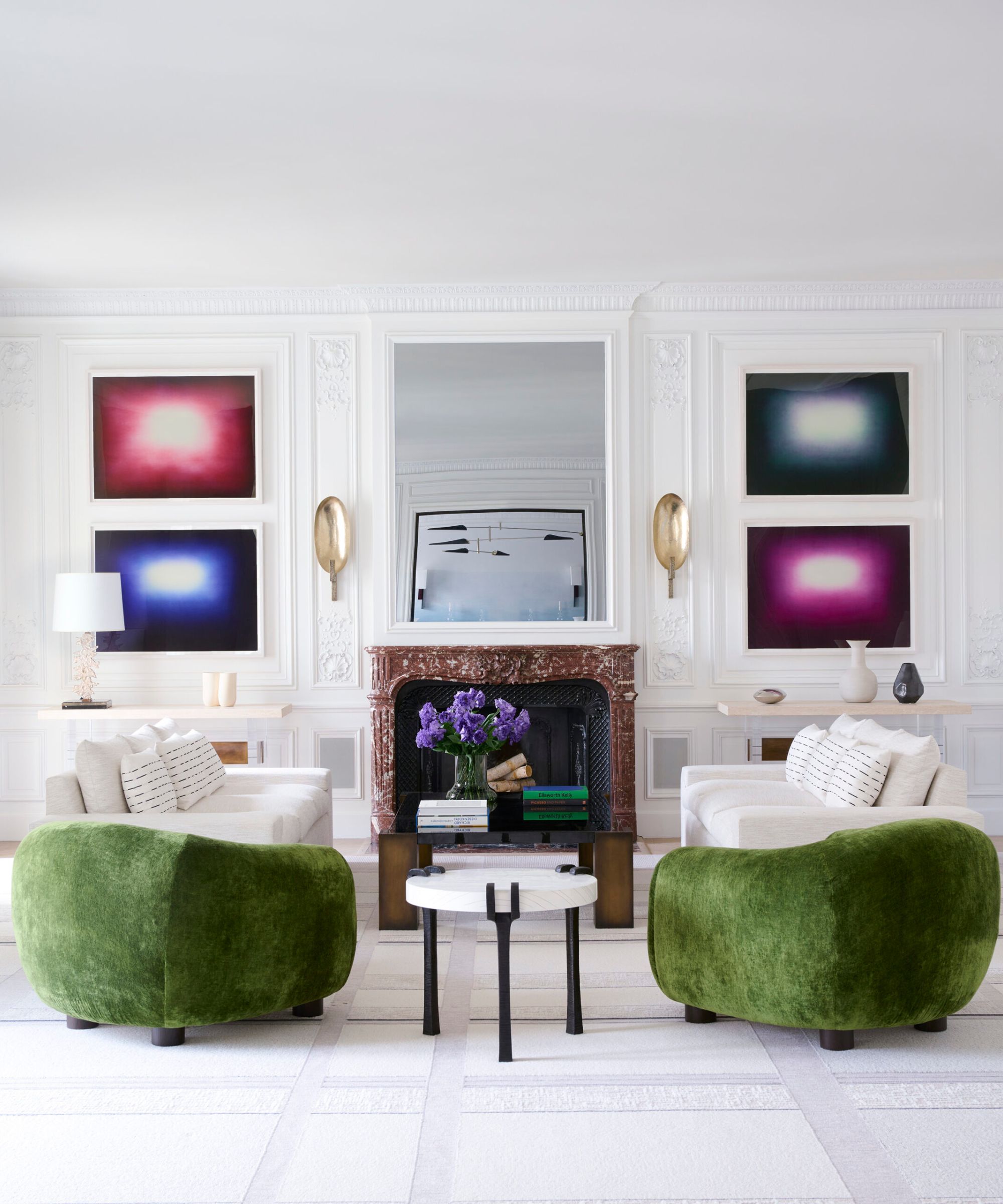 A symmetrical living room featuring two curved olive green velvet armchairs and a red marble fireplace flanked by abstract art