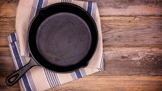 An empty cast iron skillet on a tea towel on a wooden surface