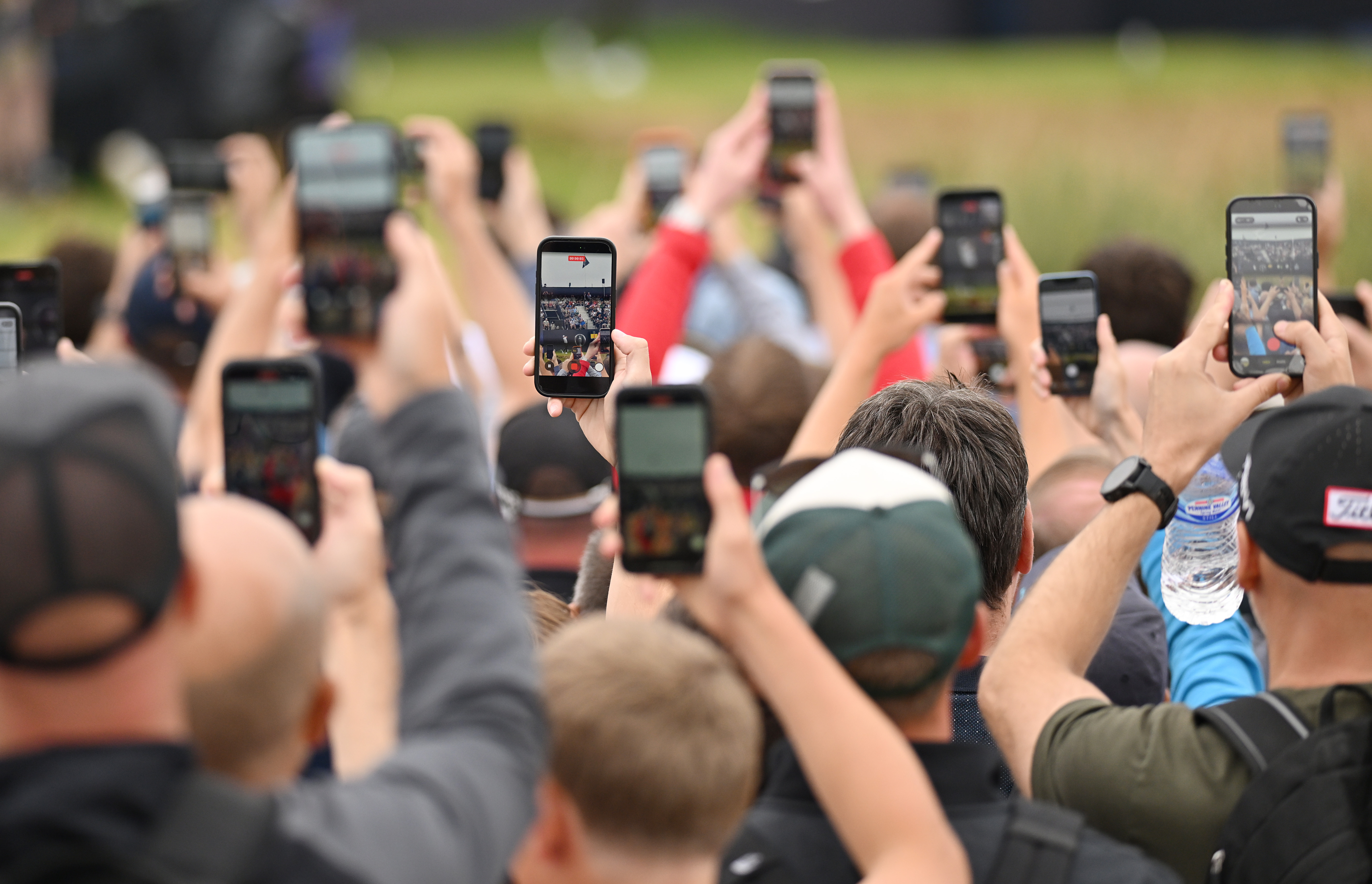 A view of golf fans holding up their phones to film at a golf tournament