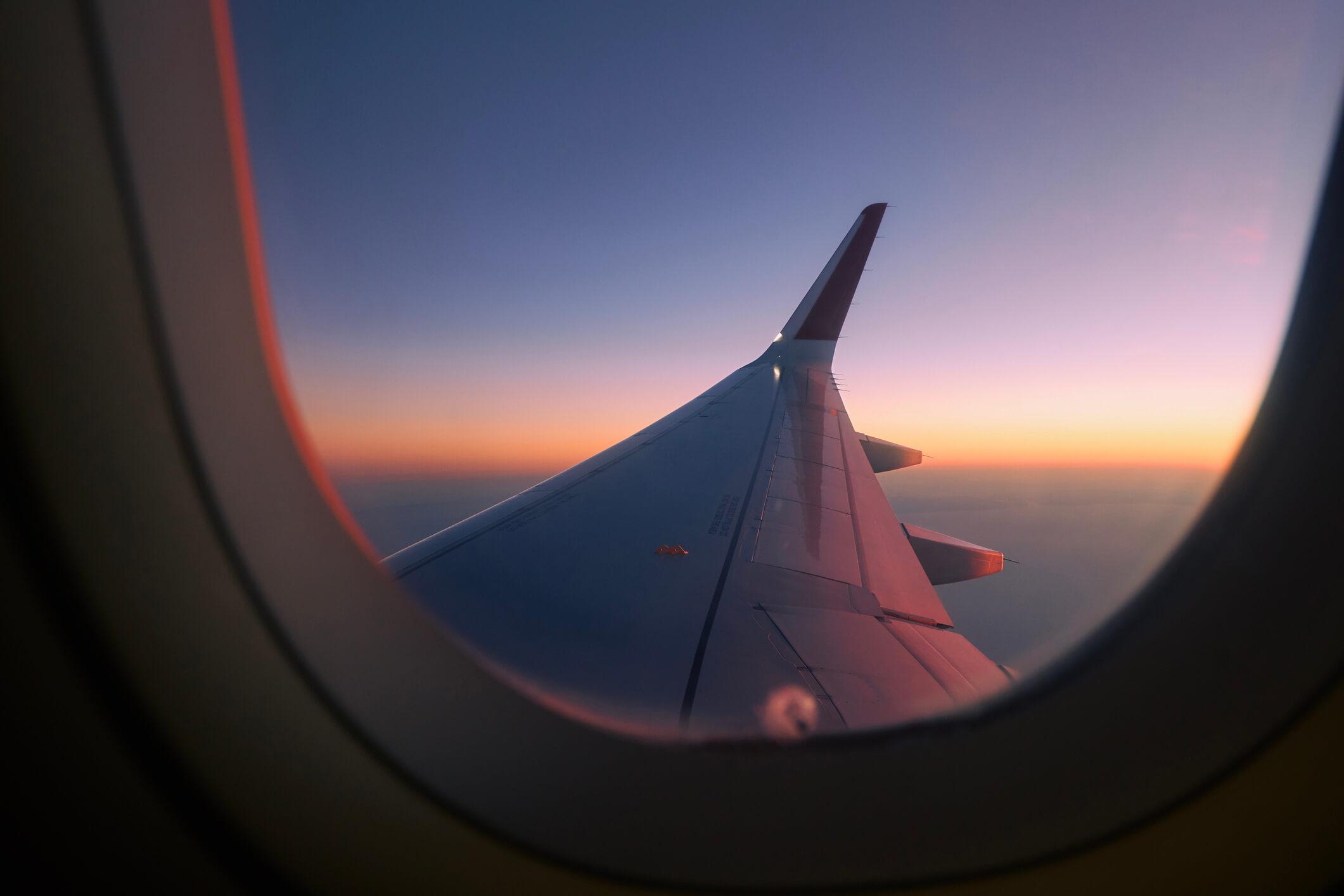  View through airplane window flight above clouds at colourful sunset. 