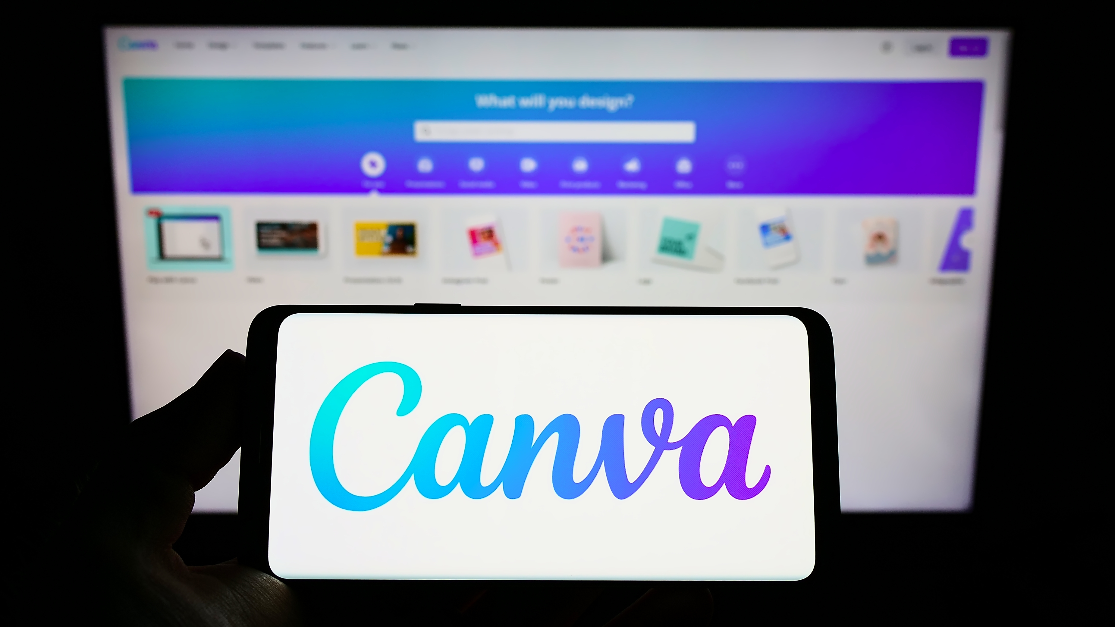 Person holding smartphone with logo of Australian graphic design company Canva Pty Ltd on screen in front of website.