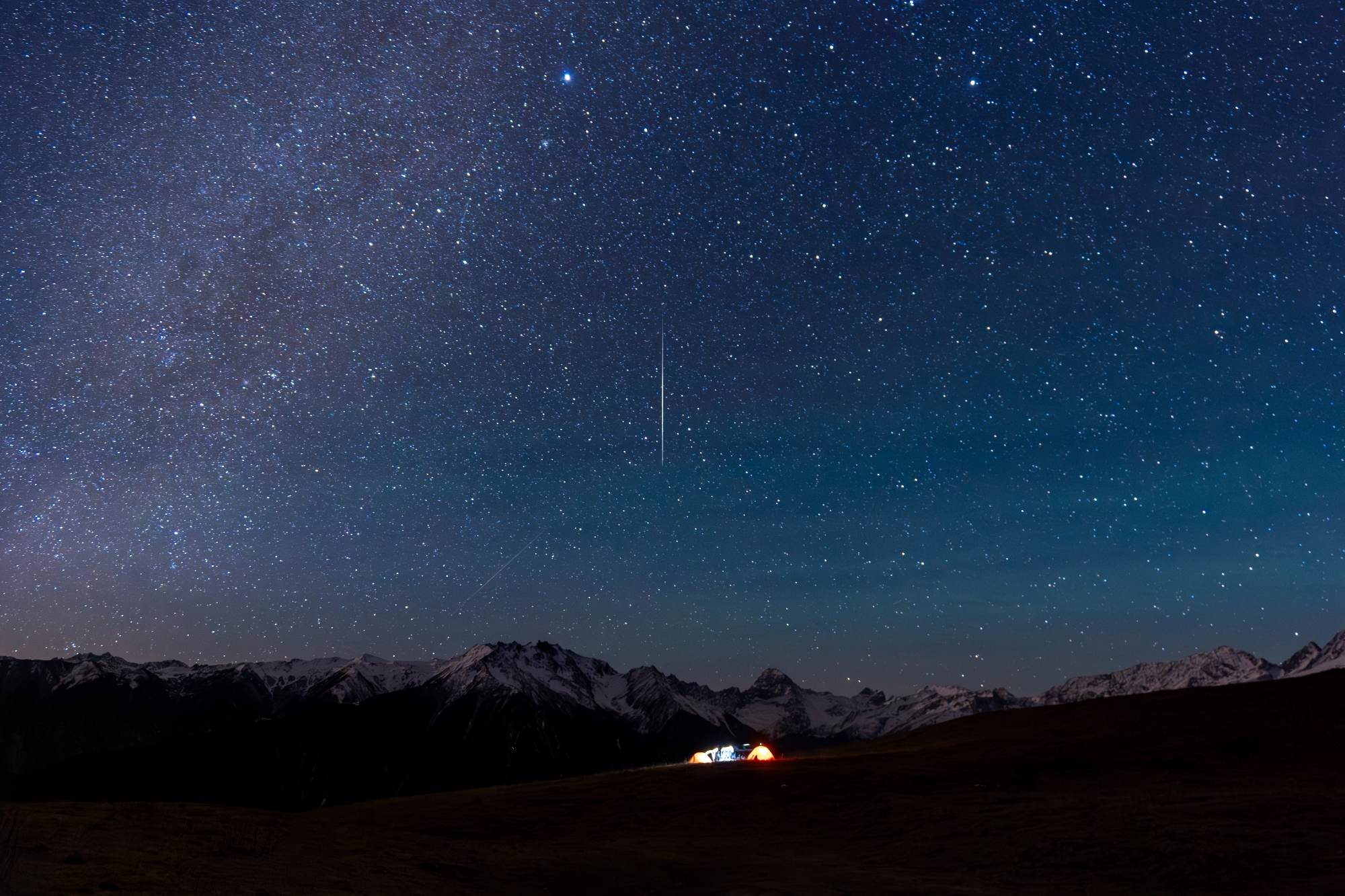 A photo of the Geminid meteor shower over a camp and mountains in China.