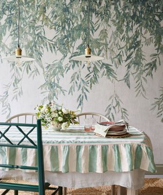 dining room with leafy botanical wallpaper and green stripe tablecloth with green chair and pendant lights