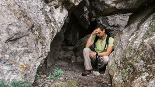 一位徒步旅行者在落基山脉长途徒步旅行后，疲惫地坐在洞穴里打盹