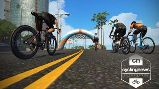 A screengrab of Zwift gameplay, showing four cyclists riding on a tarmac road underneath an inflatable banner