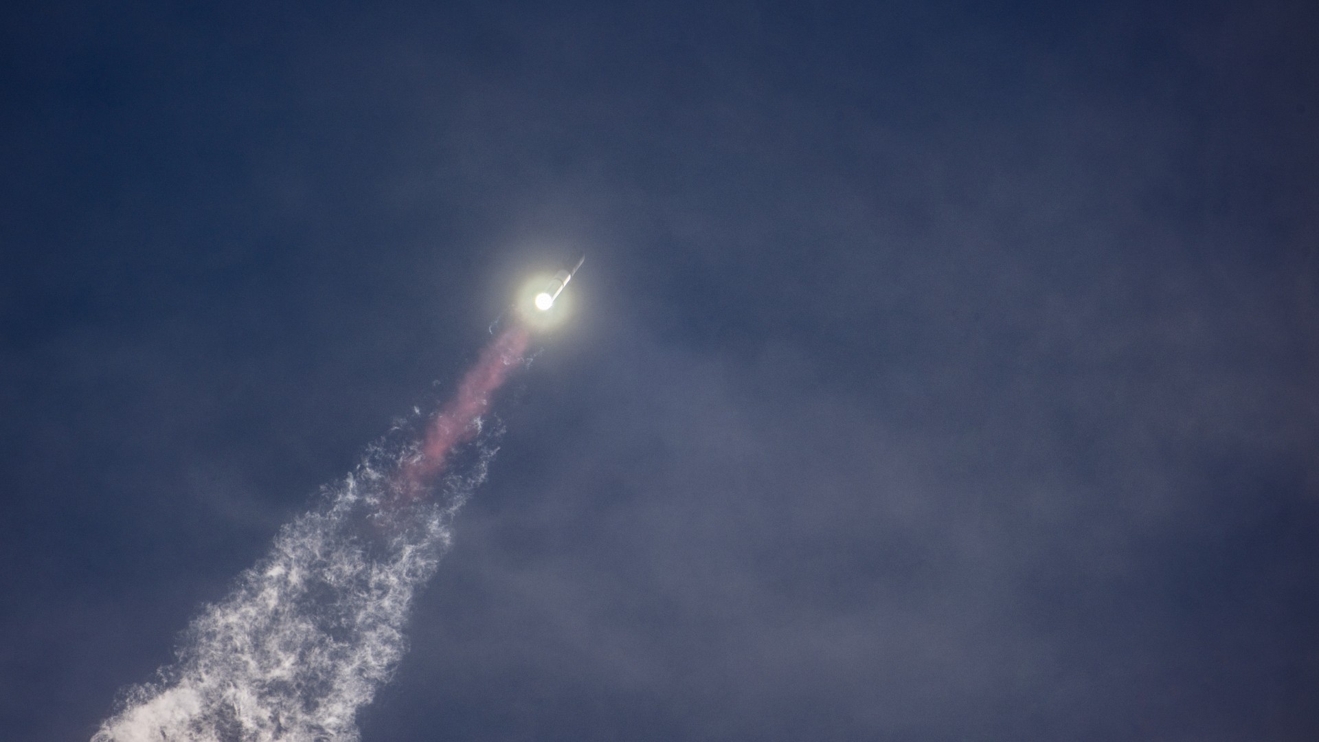 Eine große silberne Rakete fliegt über einer Flammensäule durch einen blauen Himmel