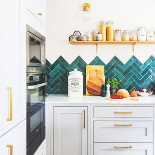 White painted kitchen with grey cabinets, white worktop with brass hardware, and teal chevron tiled splashback