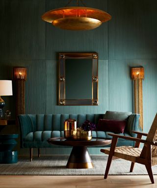 Living room with large blue panels, large golden pendant, matching golden wall lights, large rectangular mirror, blue sofa, rounded coffee table, woven armchair with wooden frame, gray rug on light wood flooring