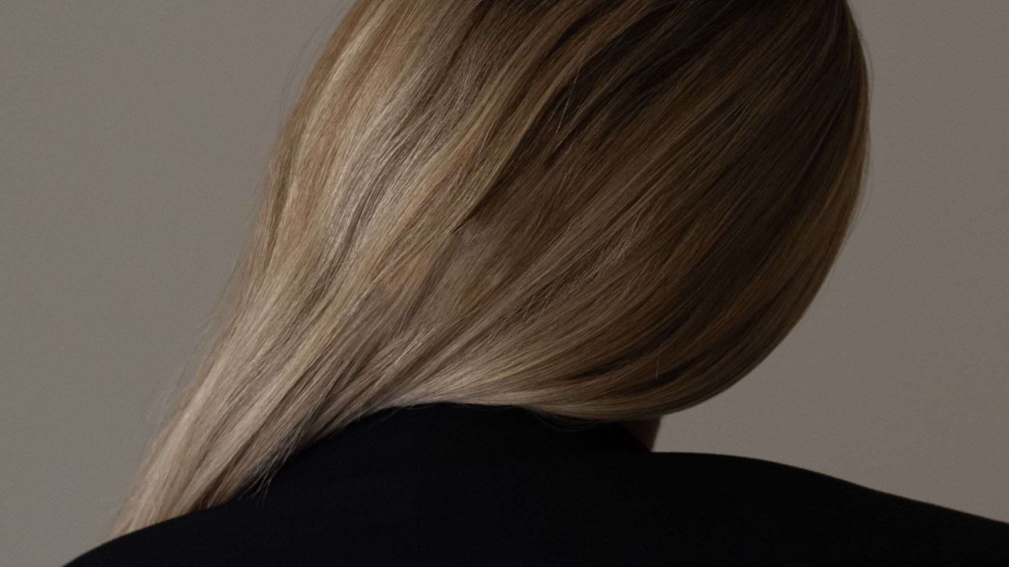 An image of a woman in a black coat with her blonde hair swept over her shoulder.