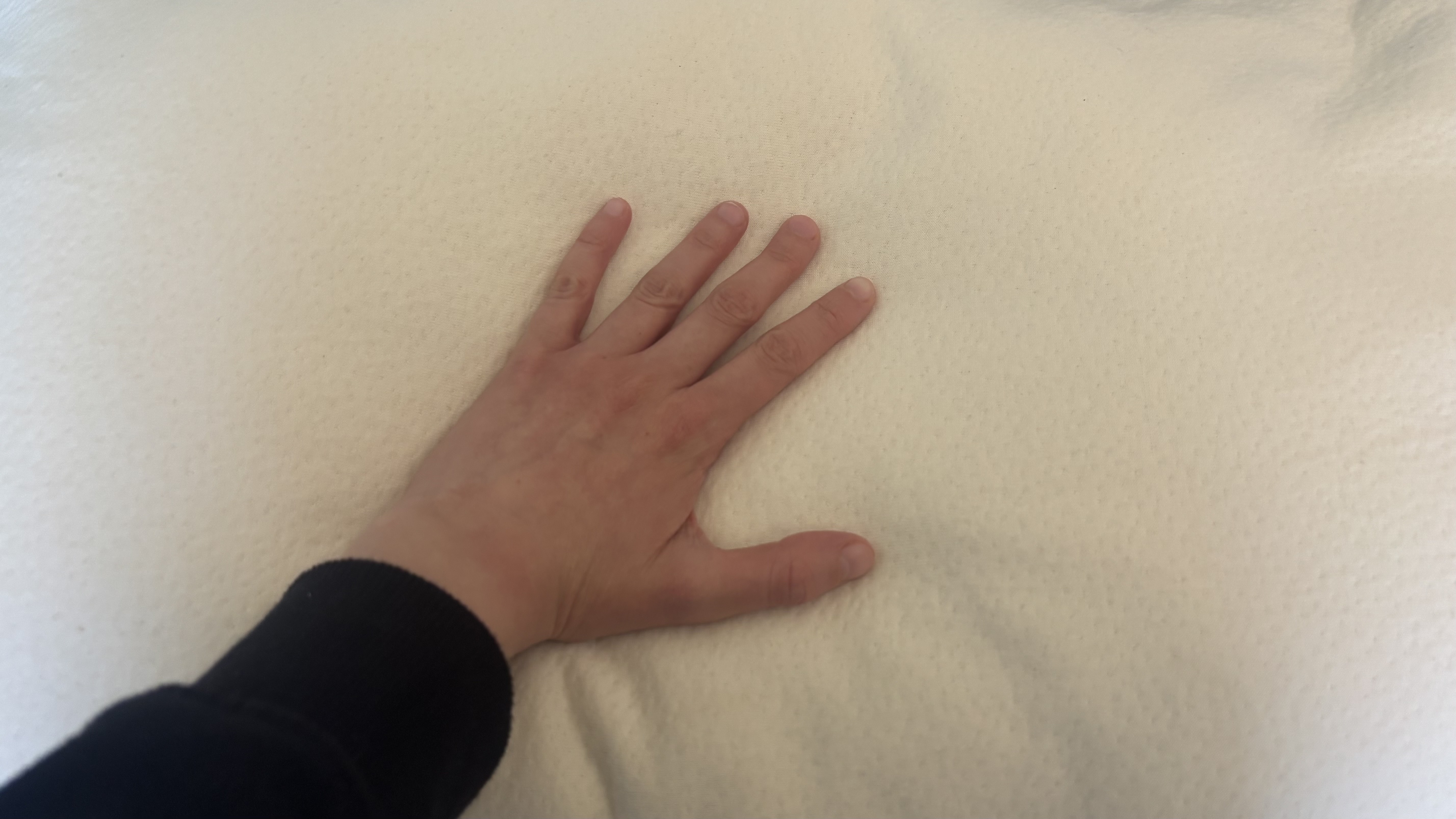 A hand tests the temperature regulation of the Birch Organic Pillow.