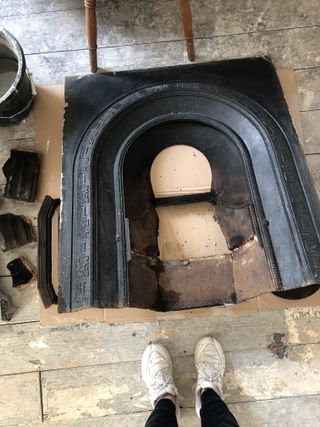 A black cast iron fireplace insert on the wooden floor of a room with a person's feet showing