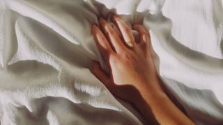 Cropped woman's hand clasping a bedsheet