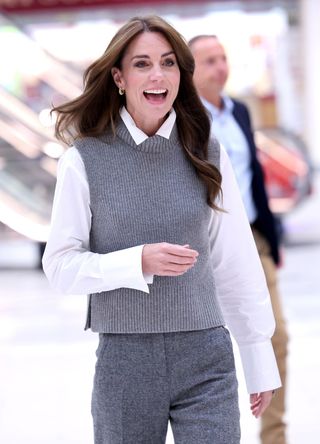 Kate Middleton wearing a grey sweater vest and grey trousers.