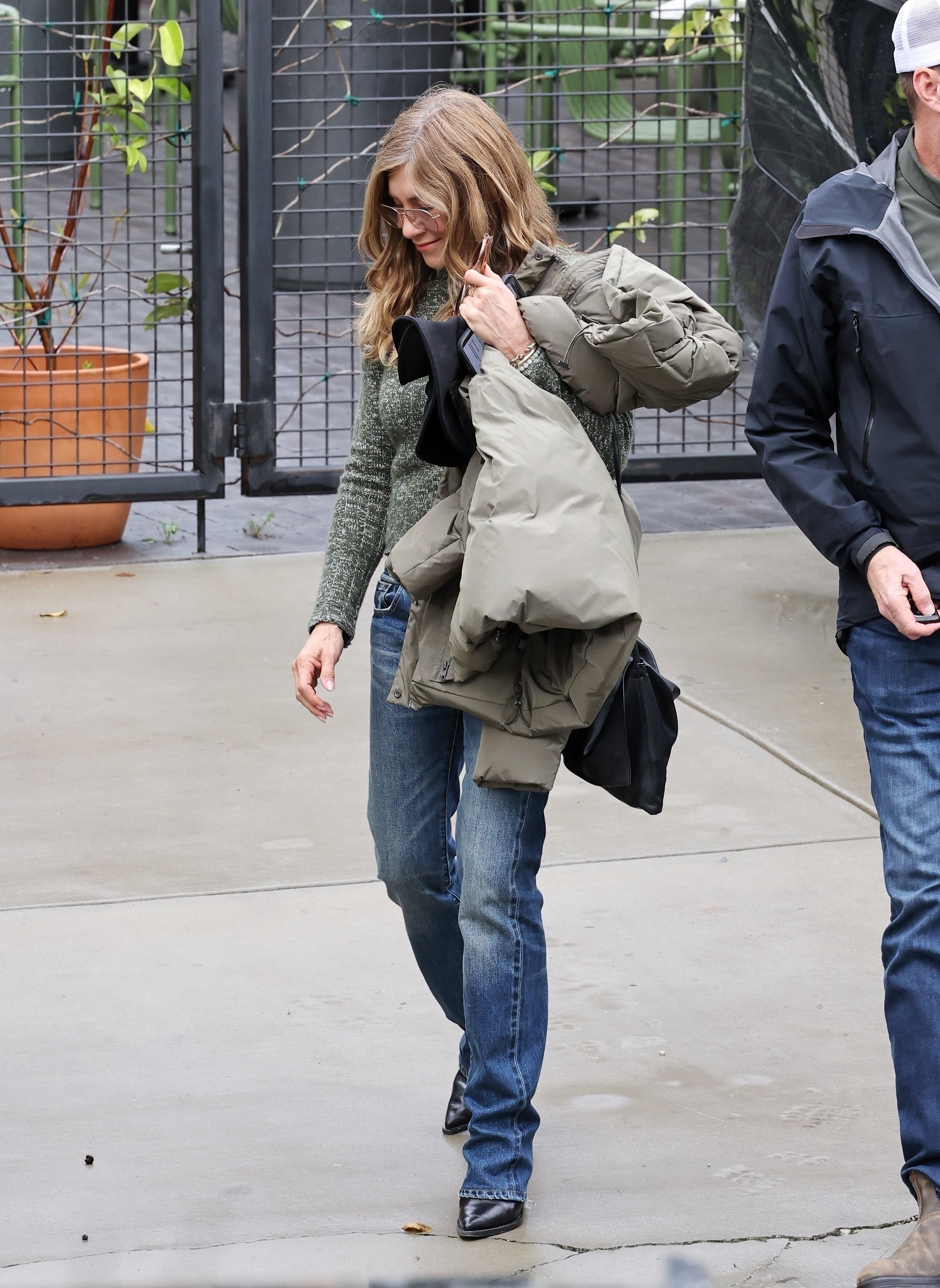 Jennifer Aniston and new boyfriend Jim Curtis at an event in Summerland, CA, wearing cigarette jeans with a green sweater and black pointed-toe boots.