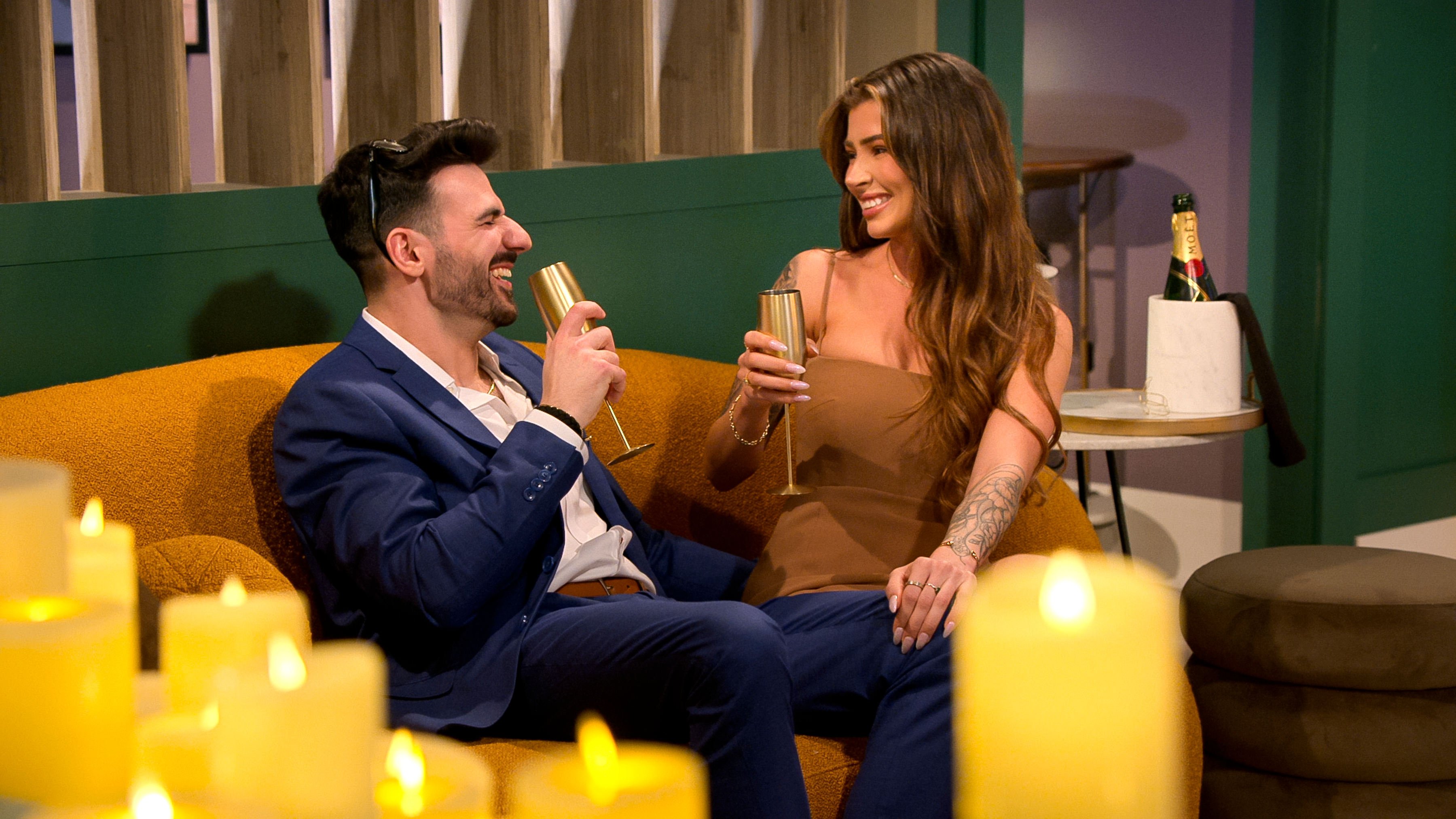 ali and anton from love is blind season 9 sit on a couch drinking champagne after their proposal