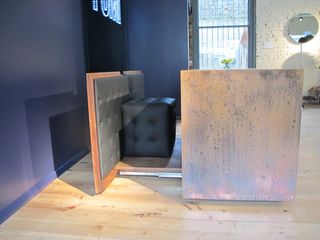 Black leather cube resting next to a brown board with grey leather padding. Photographed in a room with blue walls and wooden flooring