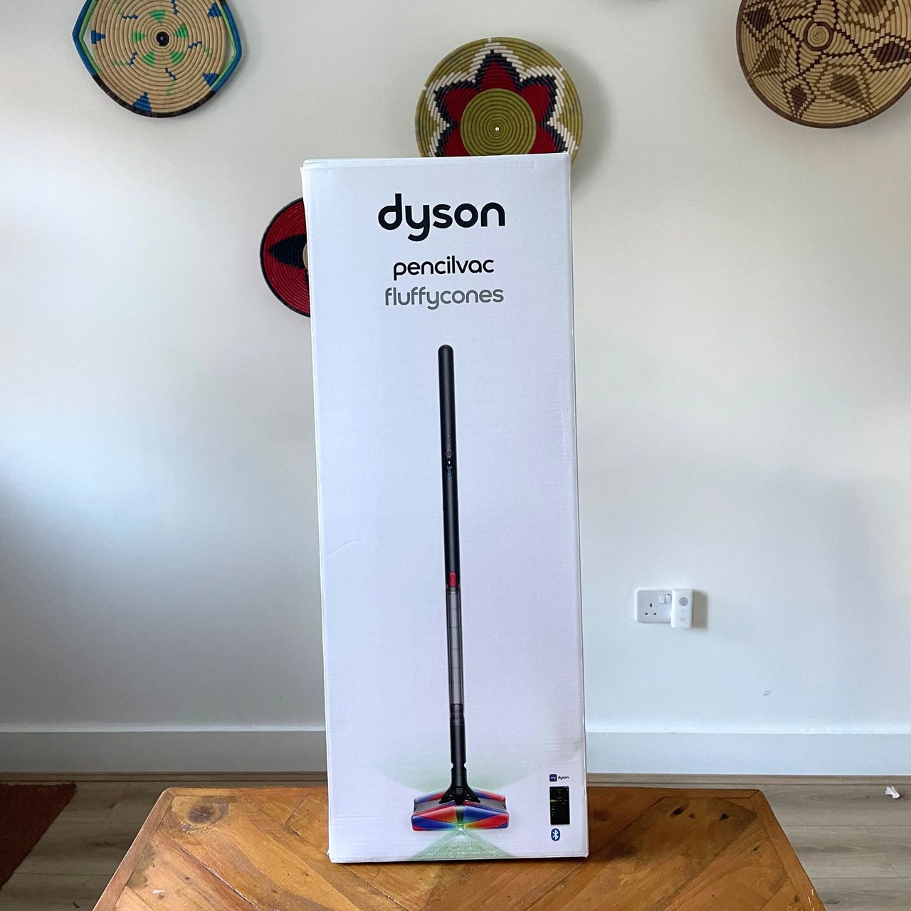 Dyson PencilVac box sitting on a wooden table in front of a white wall