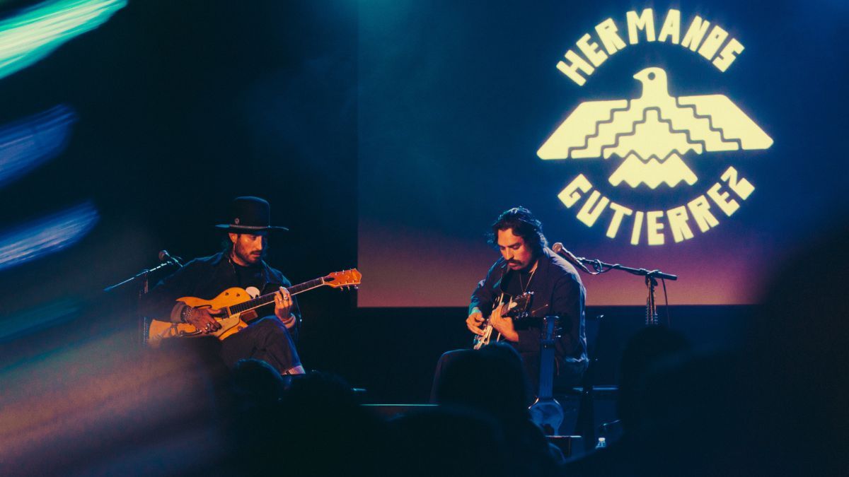 Guitar duo Hermanos Gutiérrez playing their guitars on stage with a projection of their logo at the back 