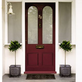 Dark red front door with two plants either side, and white painted porch