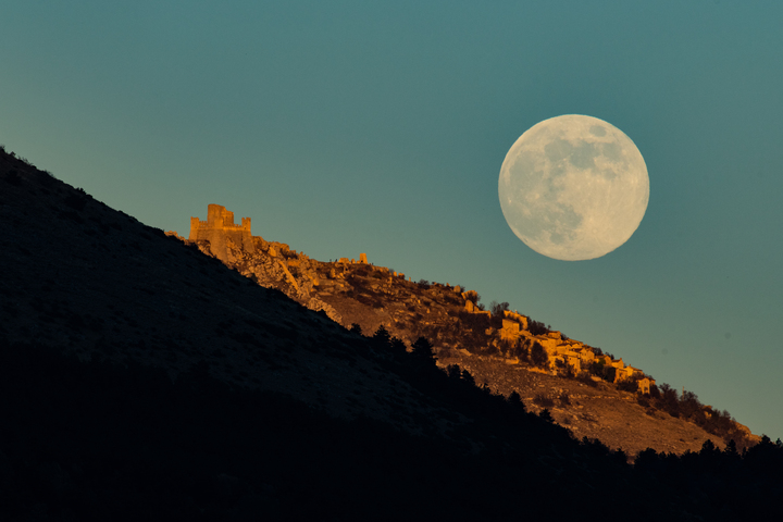 A full moon rises behind a mountain ridge
