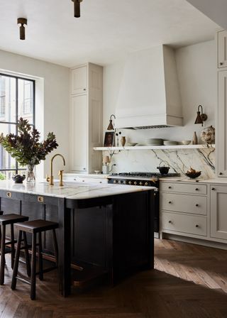 A modern white kitchen with a black freestanding island and marble backsplash