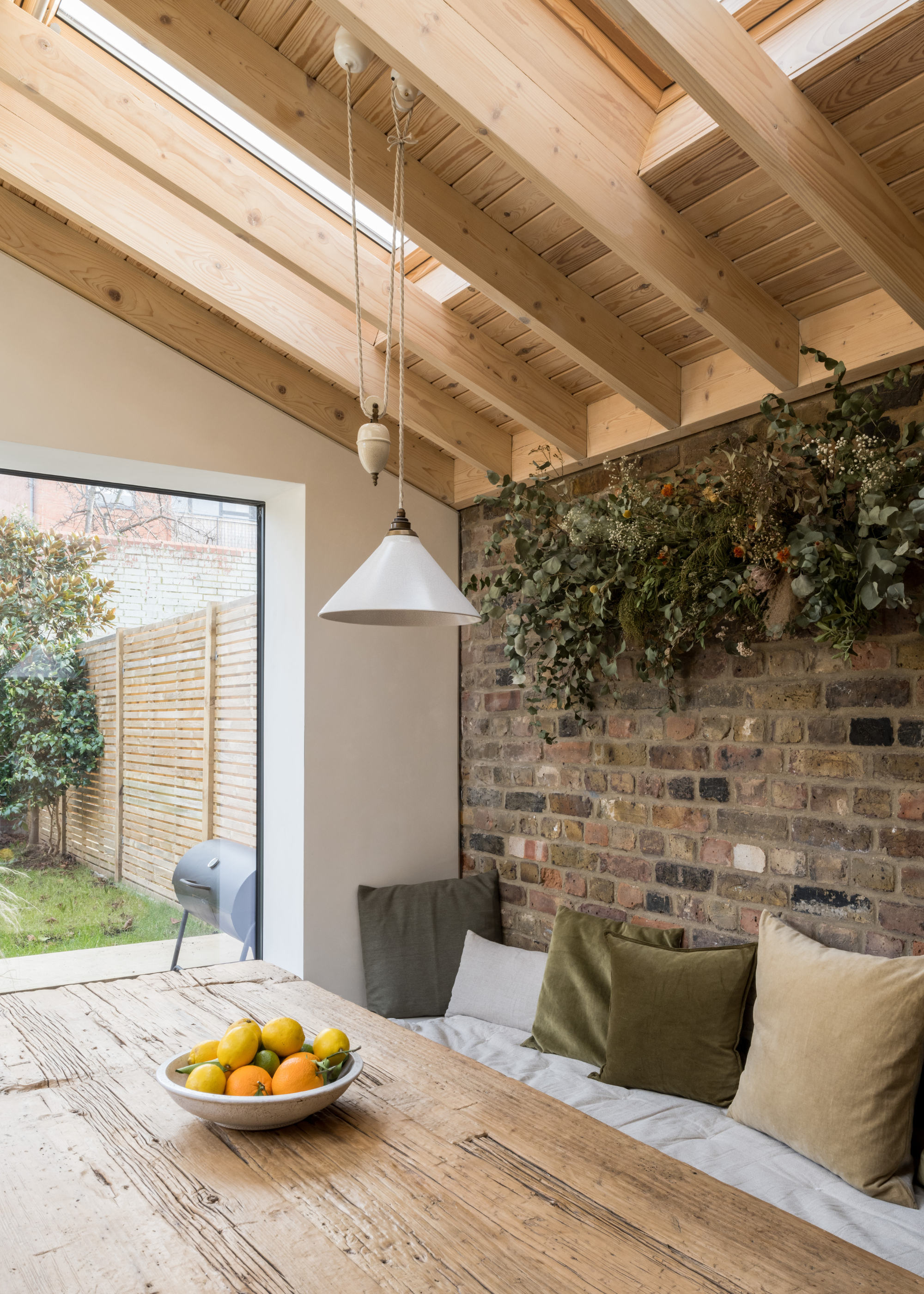 A warm dining nook with banquette seating, green pillows, a bowl of oranges and lemons, and vaulted wood ceilings