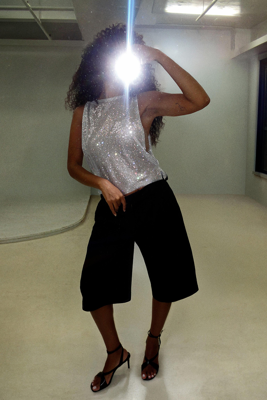 a woman wearing a sparkly top and long shorts