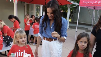 Meghan Markle wearing a blue shirt and white pants