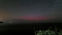 A view of the night sky over a dark ground. There are stars in the sky and there's a faint red glow lower closer to the horizon.