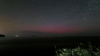 A view of the night sky over a dark ground. There are stars in the sky and there's a faint red glow lower closer to the horizon.