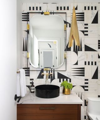 A small bathroom with a dark wood vanity, geometric black and white wall tiles, and gold hardware