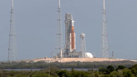 An orange and white rocket sits on a launchpad with metal scaffolding all around