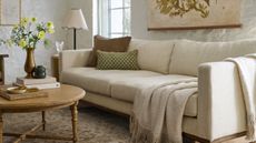 Neutral living room featuring a natural antiqued wood coffee table, cream couch, scallop bordered floor lamp, and a floral tapestry