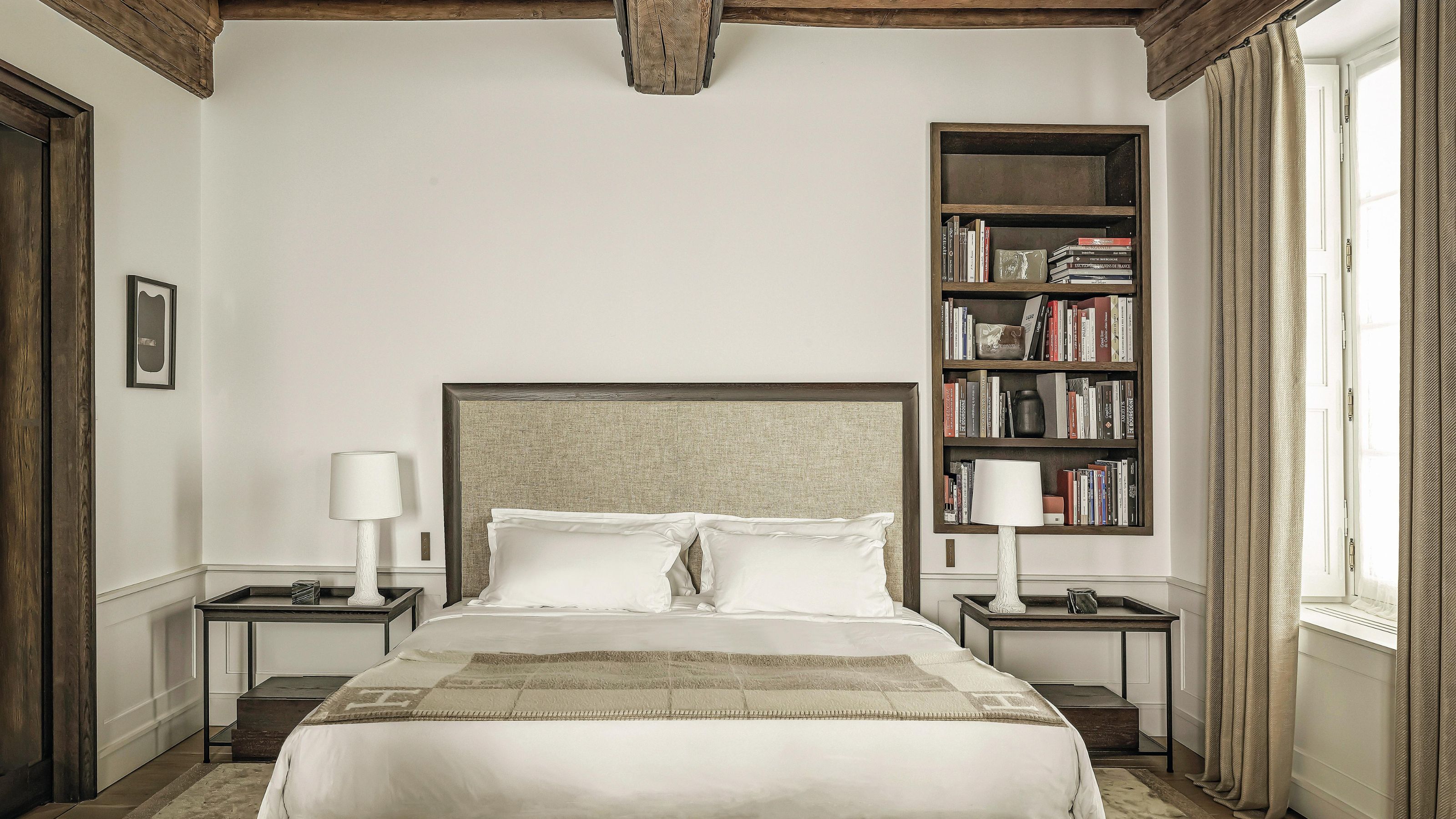 a hotel-style bedroom in a Frenc townhouse with a rustic wooden ceiling with built in bookcase