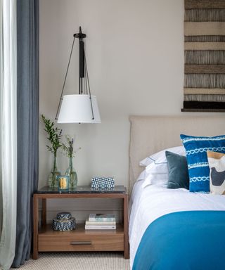 A neutral bedroom with a blue bed and an oversized wall mounted pendant bedside lamp