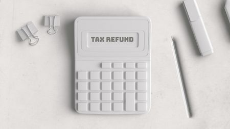 White calculator that reads "Tax Refund" next to a white pencil and some paper clips