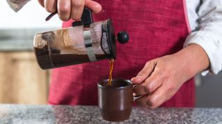 French press pouring brewed coffee into cup