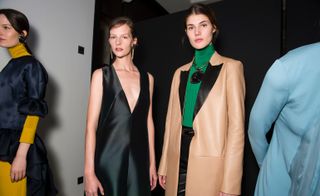 Model wears a deep V-neck black dress, another wears a beige leather jacket with black lapels and a green turtleneck