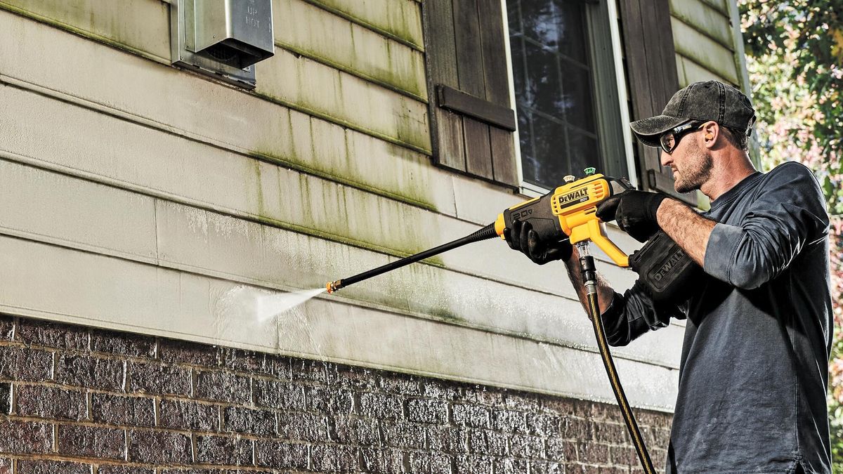 Man cleans vinyl siding with cordless dewalt pressure washer