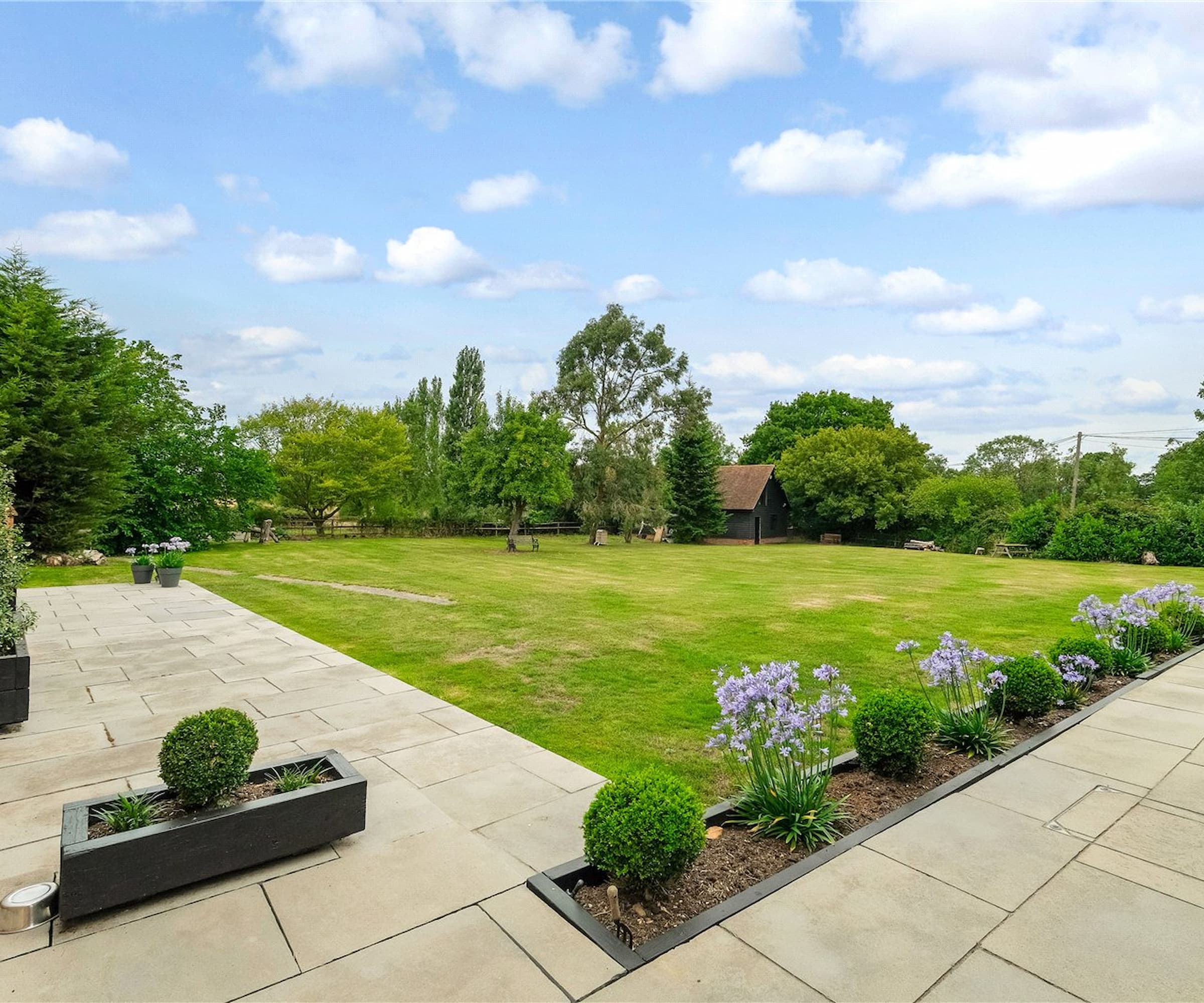 A grass garden with an outbuilding next to patio slabs and raised garden beds with wood chippings inside