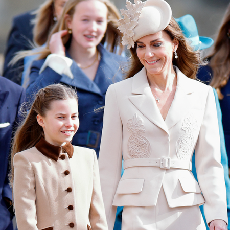 Princess Charlotte wears a tan brown coat dress and walks next to mom Kate Middleton who wears a cream ensemble
